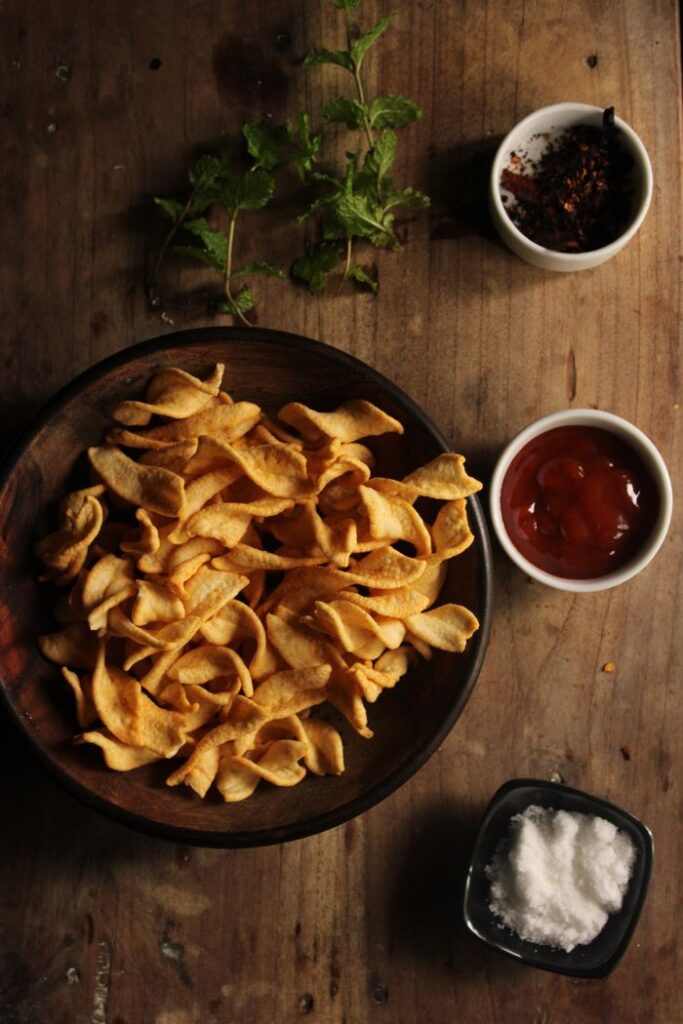 A cozy, rustic snack spread featuring crispy fried chips, dips, and fresh mint on a wooden surface.