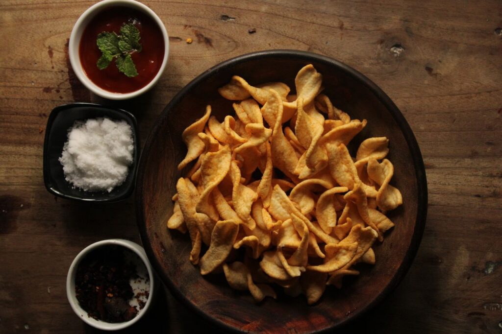 A bowl of snack chips with sauces and spices on a rustic wooden table.