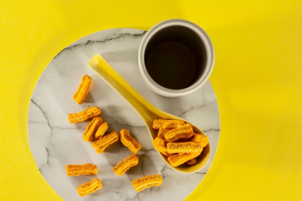 Flat lay shot of cornflakes on marble plate with a coffee mug, vibrant yellow background.