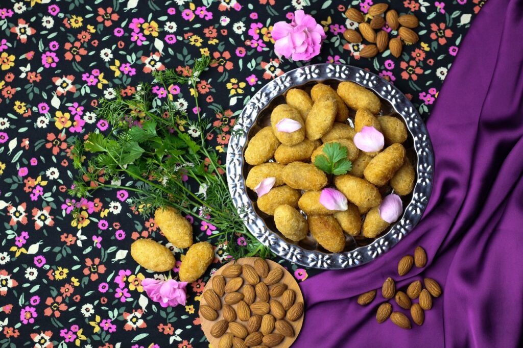 A top view of Middle Eastern pastries on a floral tablecloth with almonds and herbs.